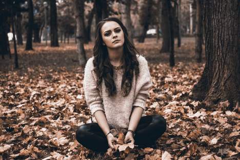 Eine traurige Frau sitzt auf dem Waldboden und überlegt sich wo sie hilfe und Beratung bei Depressionen in Frankfurt am Main bekommen könnte